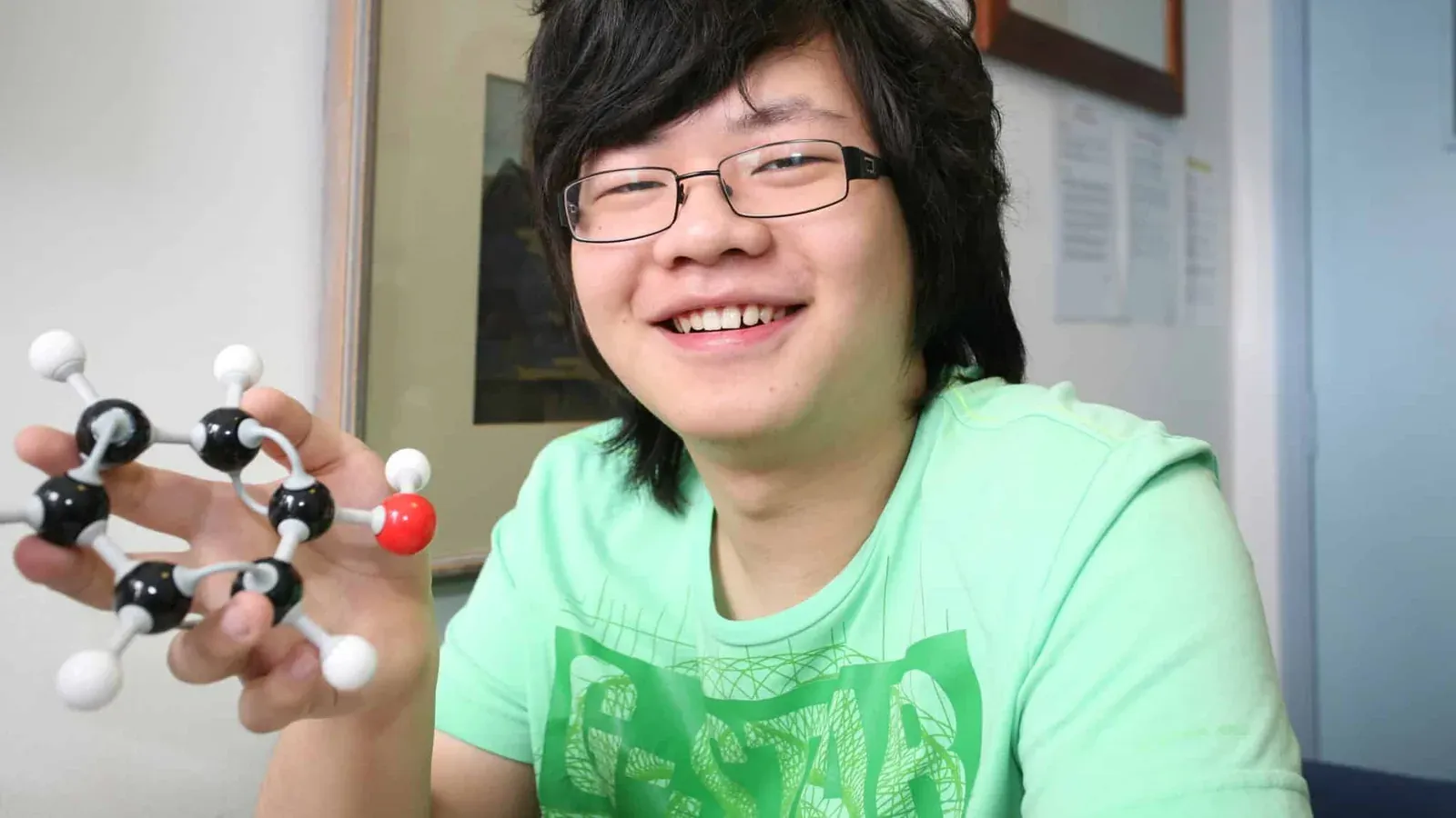 A student in a chemistry lesson holding a ball and stick model of a molecule.